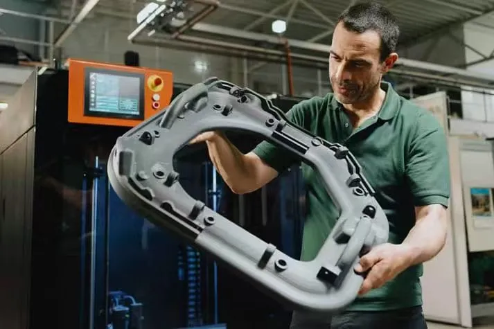 Worker holding large SLS 3D‑printed industrial part in manufacturing plant
